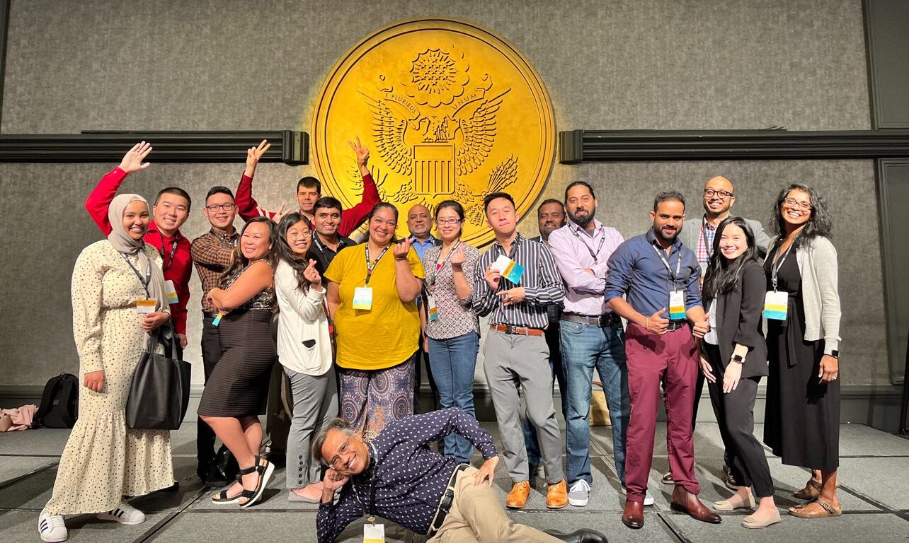 Candid group photo of NAAAP attendees posing playfully in front of a large gold ceremonial seal backdrop, Leadership Convention, Washington DC, August 2022.