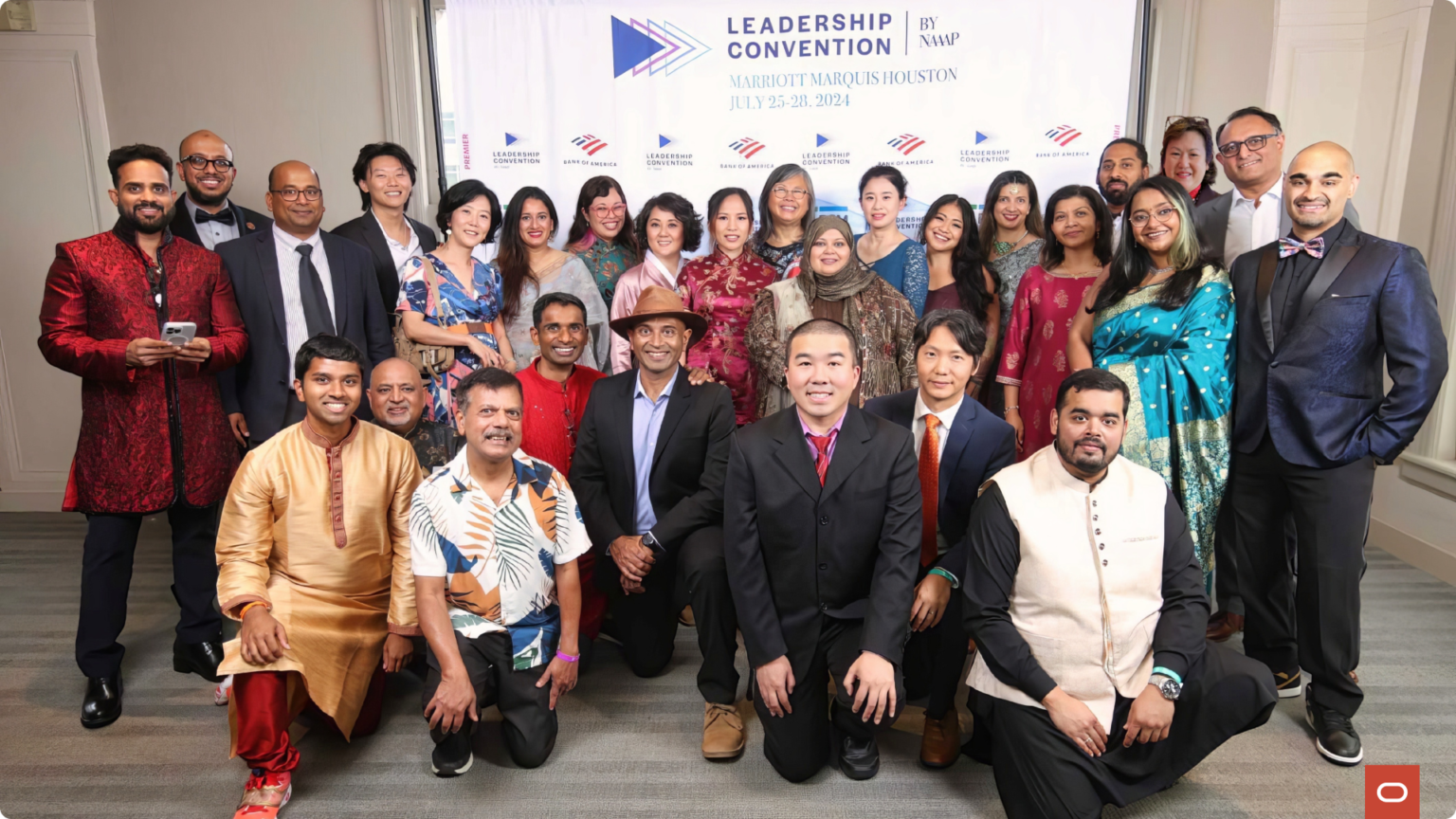 Large formal group photo in front of a Leadership Convention by NAAAP step-and-repeat banner with sponsor logos, attendees in mixed formal and cultural attire, Houston, July 2024.