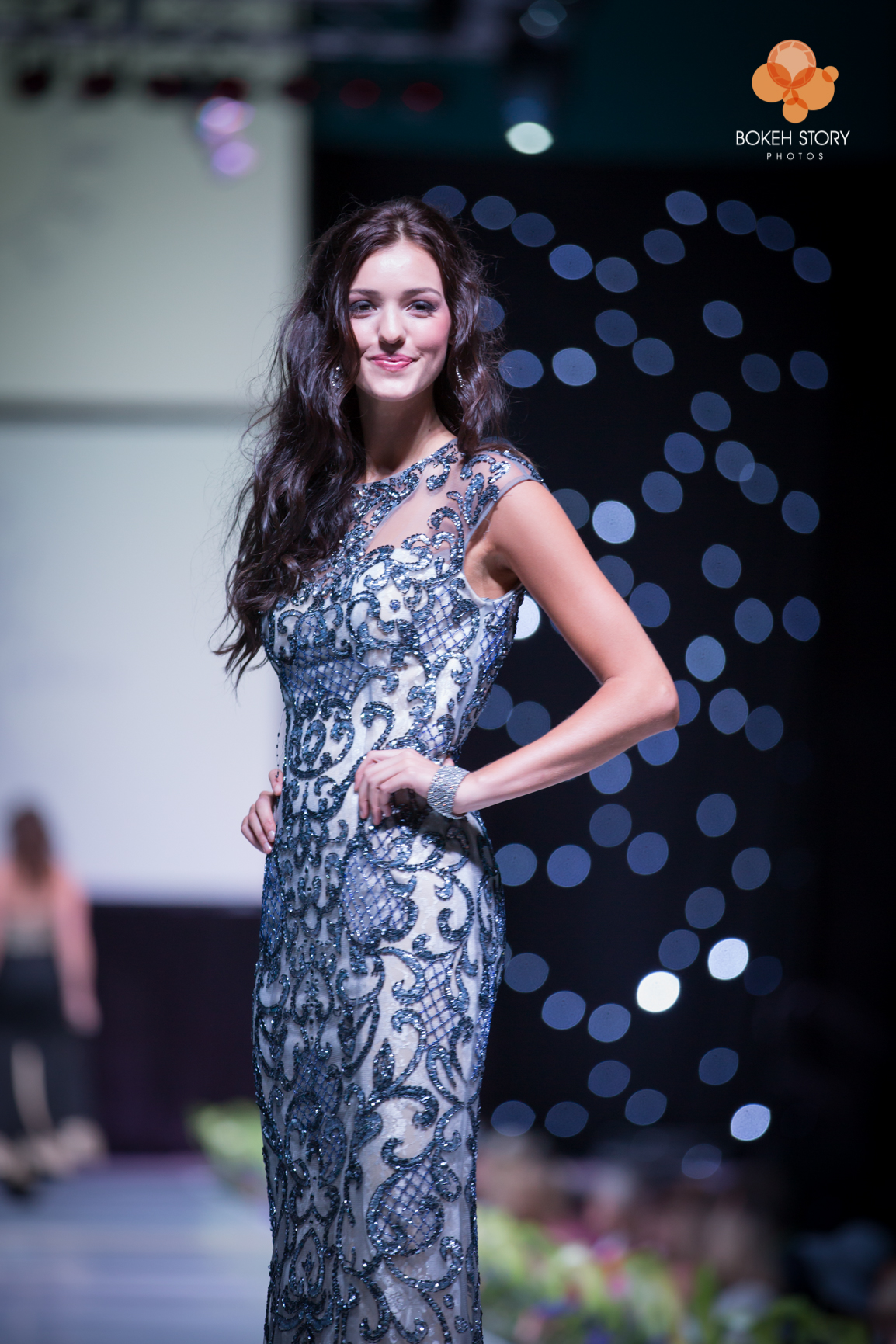 Runway photo of a model in a sequined navy and silver gown posing with a hand on her hip, Adorn Style Show.