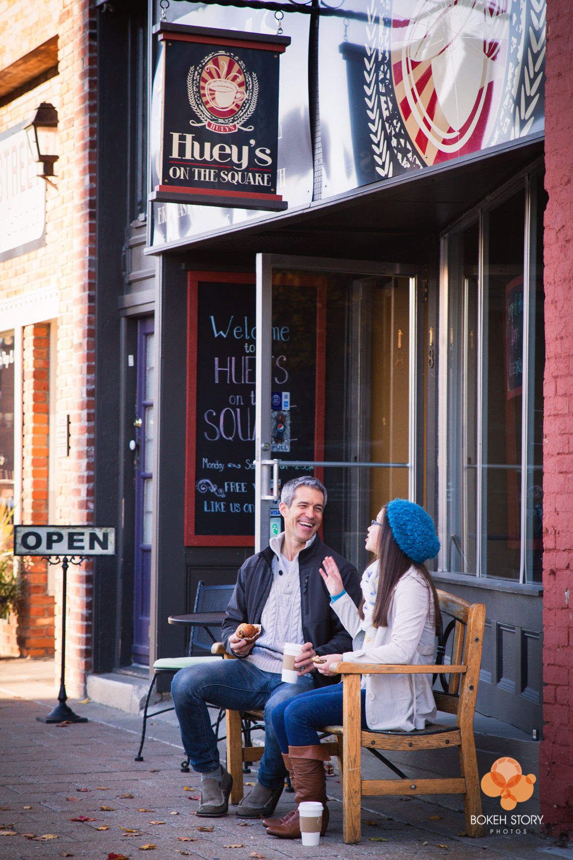 Portfolio portrait of a father and daughter laughing together on a bench outside a coffee shop storefront.