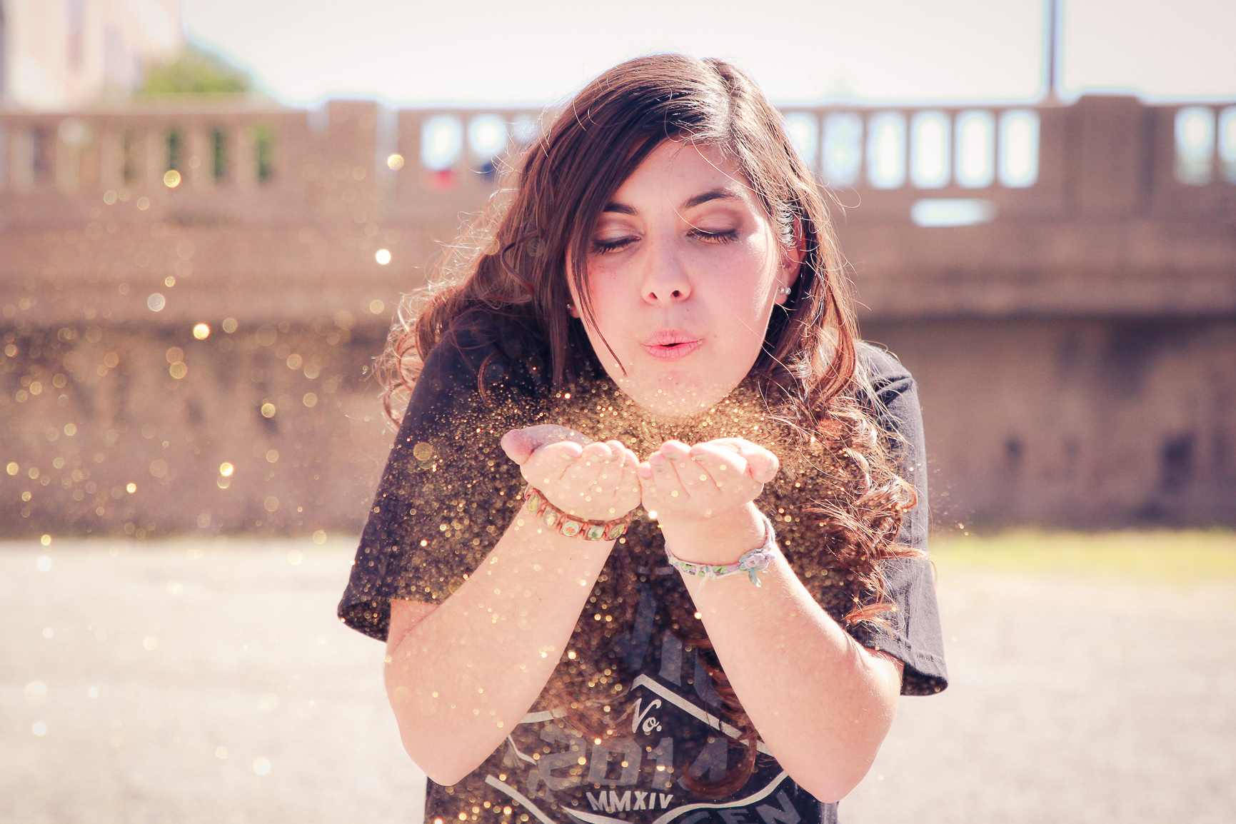 Senior portrait of a young woman blowing gold glitter from her hands outdoors.