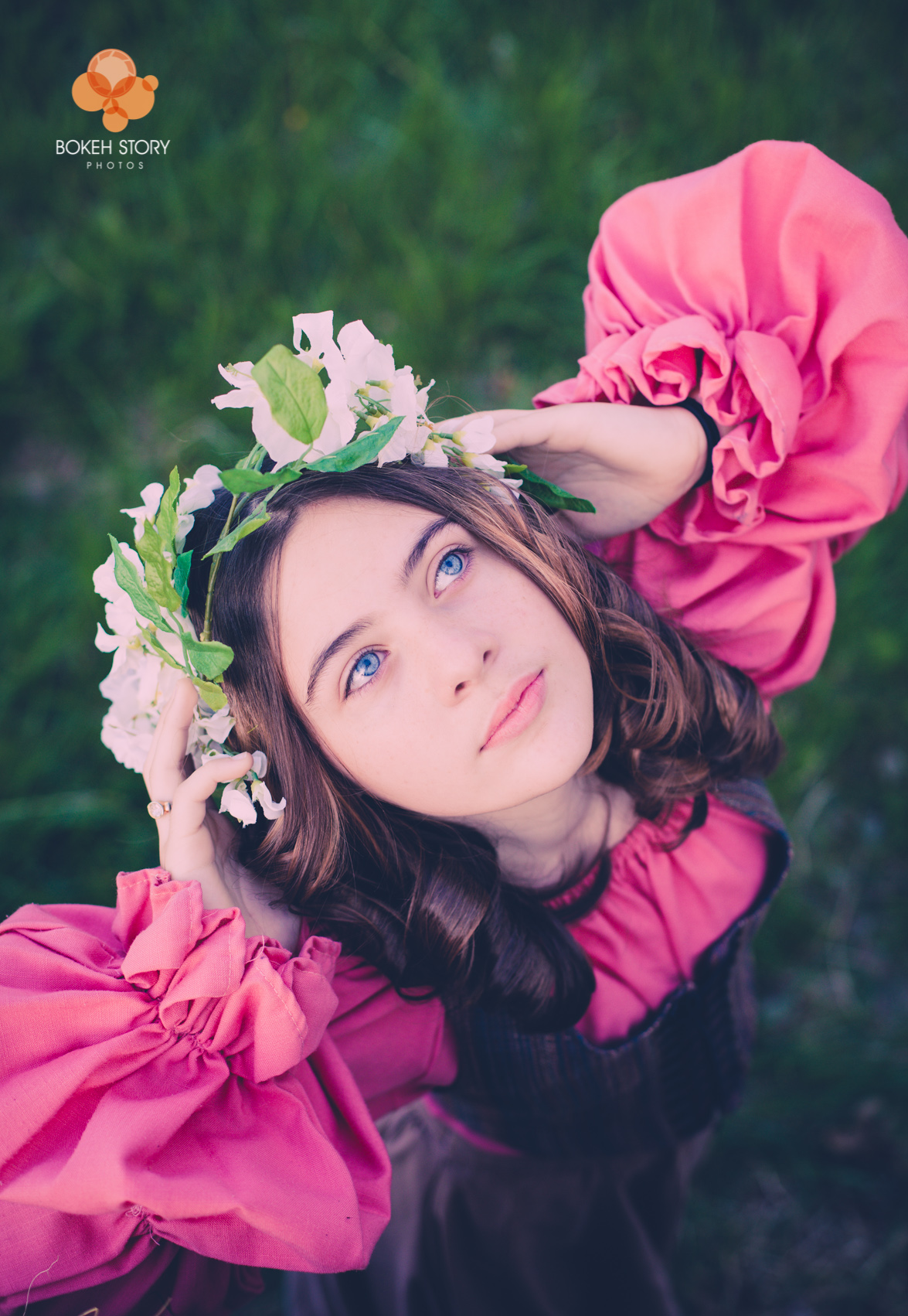 Senior portrait of a young woman in a pink dress and flower crown looking upward, close-up outdoor portrait.